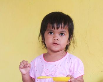 Portrait of cute girl holding yellow wall