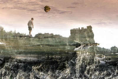 Reflection of man walking on rock in sea against sky