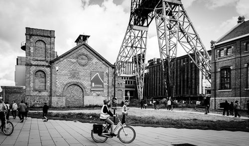 People riding bicycle on street against buildings in city