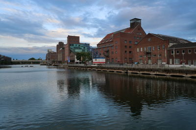 Buildings by river against sky