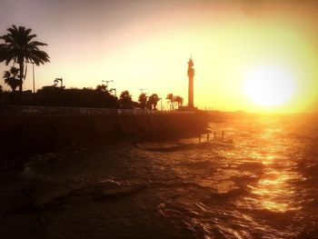 Silhouette palm trees by sea against sky during sunset