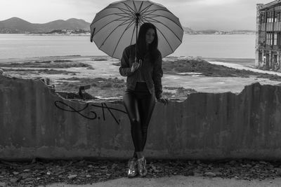 Woman with umbrella leaning on broken wall against lake in city