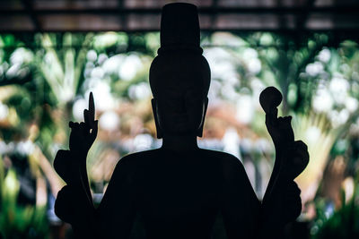 Rear view of silhouette man holding cross against blurred background