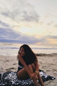 Woman smiling at beach against sky during sunset