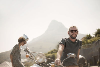 Mid adult man sitting on motorcycle with female friend during sunny day