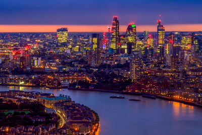 Illuminated city by river against sky