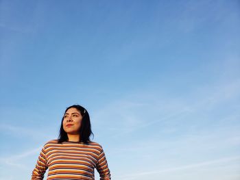 Portrait of young woman standing against blue sky