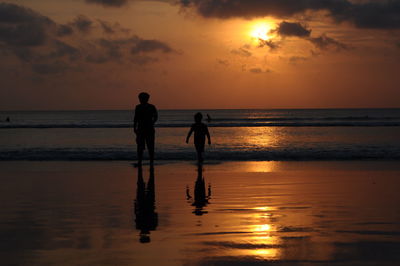 Silhouette people walking on beach against sky during sunset