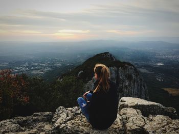 Woman sitting on rock against sky