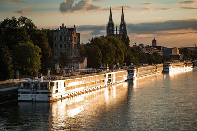 Buildings by river against sky during sunset
