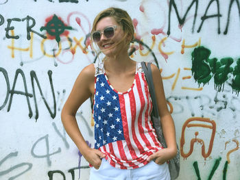 Young woman wearing american flag tank top while standing against graffiti wall