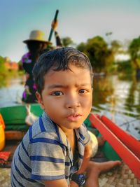 Portrait of cute boy sitting in boat with woman rowing in background