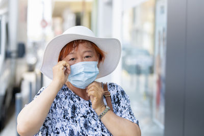 Portrait of mature woman wearing flu mask and hat standing outdoors