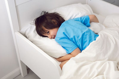 Child boy lies in a white children's bed with a blanket in a room