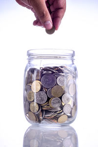 Close-up of human hand holding jar against white background