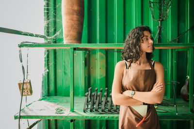 Beautiful young woman standing against green barrel at pottery shop