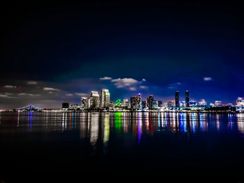 Illuminated buildings by river against sky at night