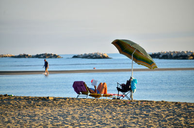 People sitting on beach by sea against sky