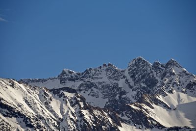 Low angle view of snowcapped mountains against clear blue sky