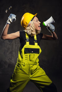 Female construction worker shouting on megaphone while standing against wall