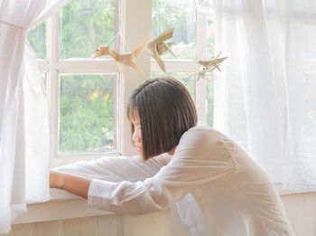 Side view of teenage girl looking through window at home