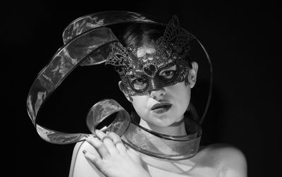 Portrait of woman holding mask against black background