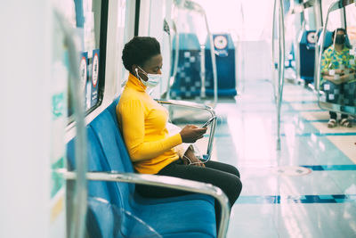 A young african woman in a protective mask rides the subway and listens to music with headphone