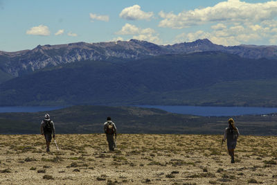 Rear view of people walking on mountain against sky