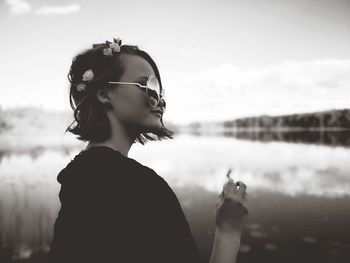 Side view of young woman standing by lake against sky