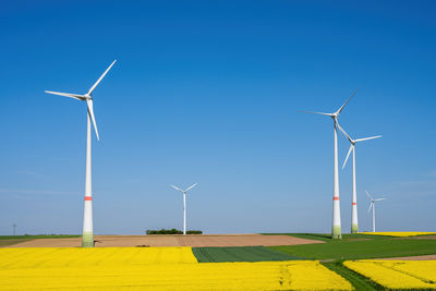 Windmills on field against clear blue sky