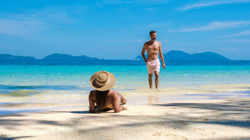 Rear view of woman standing at beach against sky