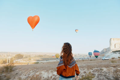 Rear view of woman with balloons against sky