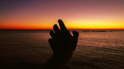 Close-up of silhouette hand against sea during sunset