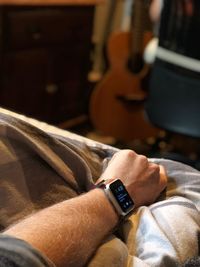 Cropped hand of man wearing smart watch on bed