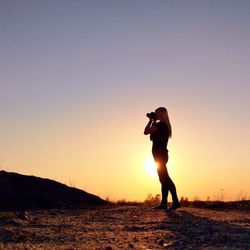 Silhouette woman photographing landscape at sunset