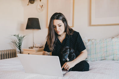 Young woman on the computer in cozy bedroom at home with dog