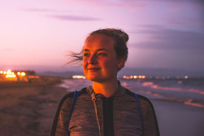 Portrait of young woman standing at beach against sky