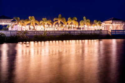 Illuminated bridge over river by buildings against sky at night