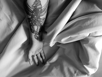 Cropped hand of woman with tattoo on bed