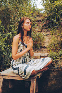 Woman practicing yoga on pier by river. young female wearing dress in lotus pose. 