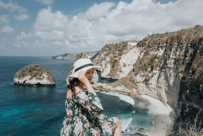 Woman standing on rock by sea against sky