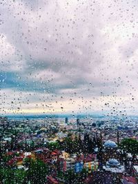 Aerial view of city against sky seen through wet window