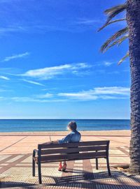 Rear view of woman sitting on bench against sea and sky