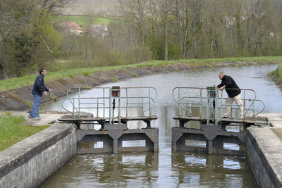 Side view of man standing on footbridge over lake