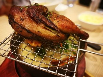Roast chicken on metal grate over earthen hot pot on table