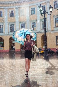 Full length portrait of cheerful woman walking with umbrella at fountain