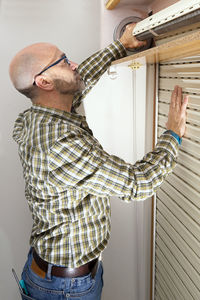 Side view of mature man holding curtain at home