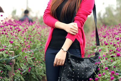 Midsection of woman with black purse standing amidst pink flowers on field