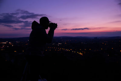 Silhouette man photographing cityscape against sky at night