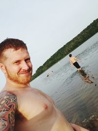 Portrait of shirtless man standing in water against sky